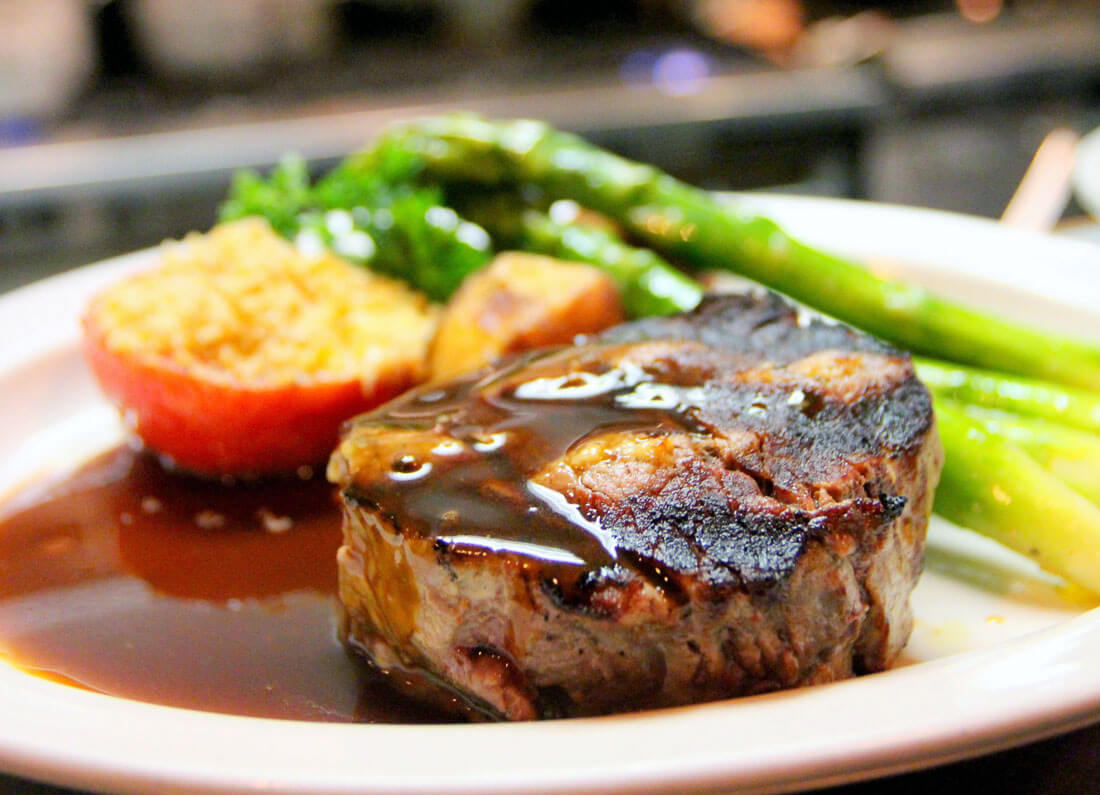 Grilled steak cooking on a grill with healthy vegetables on the side