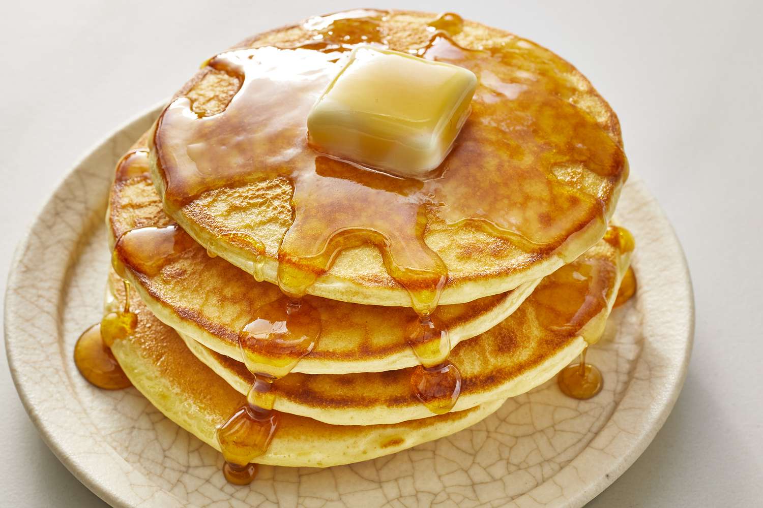 Fluffy pancakes stacked on a plate with syrup and berries.